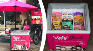 Small cart-sized freezers with pink sides and clear tops through which packaged ice cream sandwiches are visible.