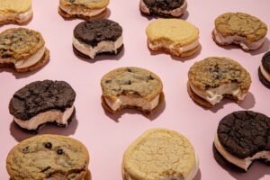 Several ice cream cookie sandwiches on a light pink background. A small bite is taken out of each one.